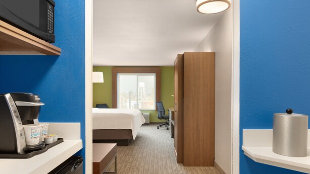 A hotel room with a bed, a desk with a coffee maker, a microwave, and a view of the city through a window. - Holiday Inn Express Hotel & Suites Merced by IHG (Merced)
