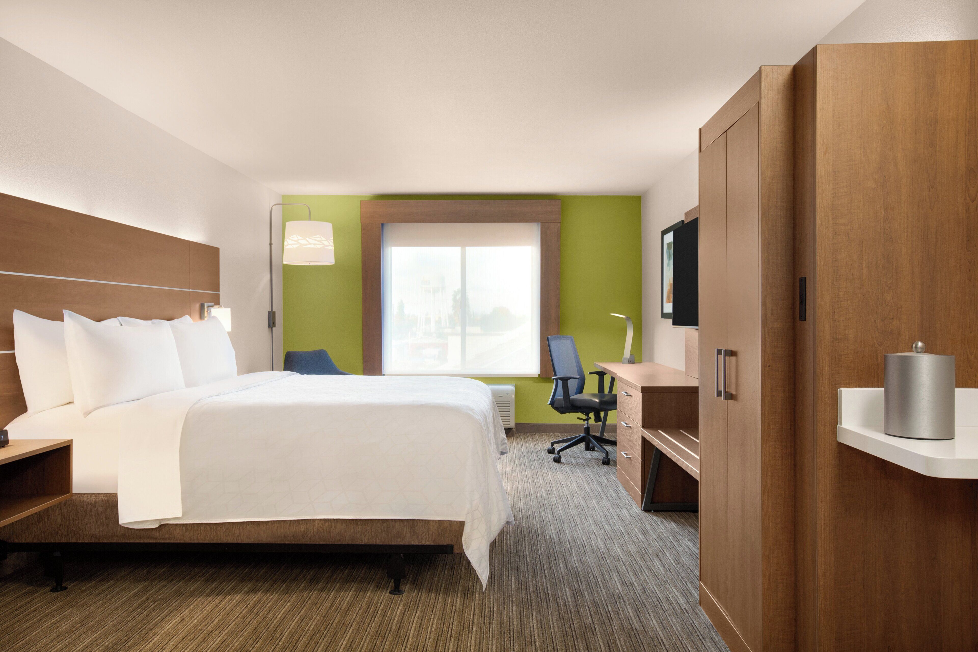 A hotel room with a bed, desk, chair, wardrobe, and a television.