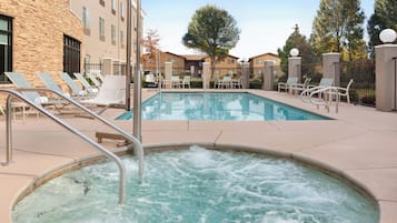 A pool area with lounge chairs, a hot tub, and a building with stone and stucco exterior.
