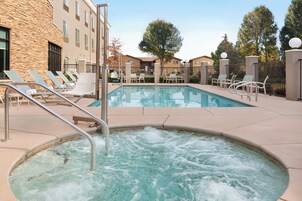 A pool area with lounge chairs, a hot tub, and a building with stone and stucco exterior.