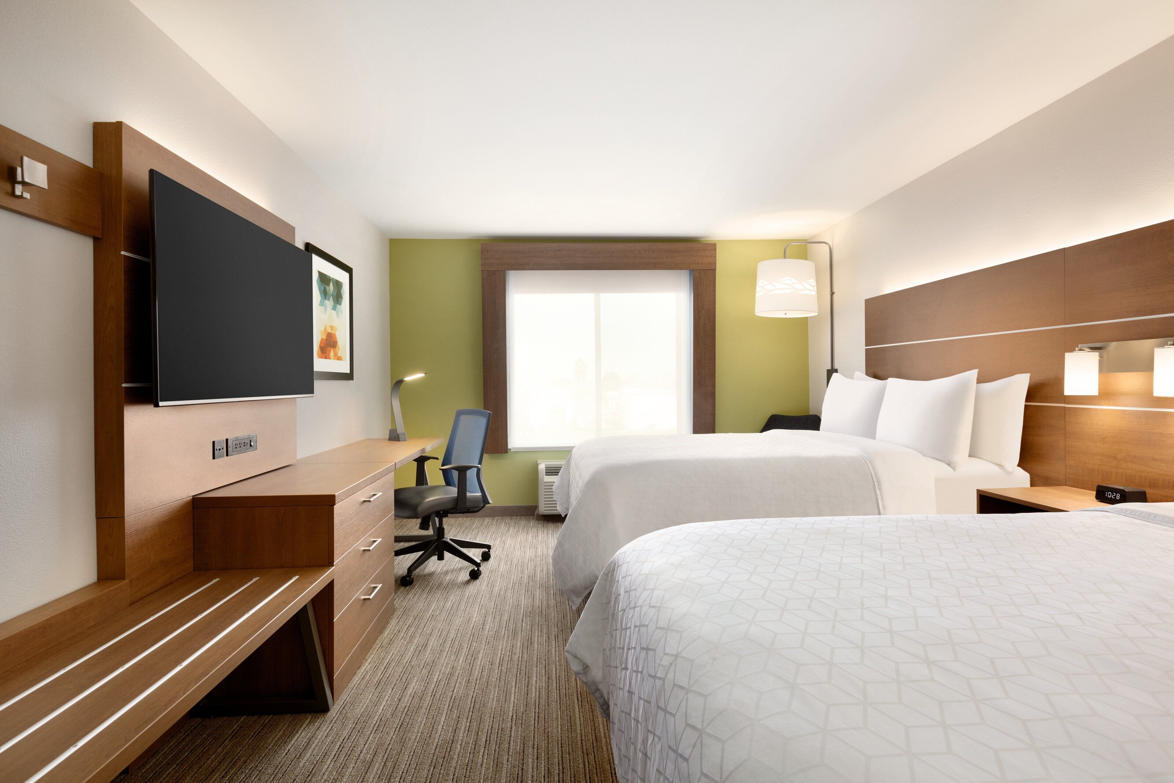 A hotel room with two beds, a desk, a chair, a TV, and a window with blinds.