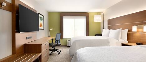 A hotel room with two beds, a desk, a chair, a TV, and a window with blinds.