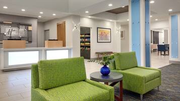 A hotel lobby with green upholstered chairs, a reception desk, and a wall-mounted artwork.