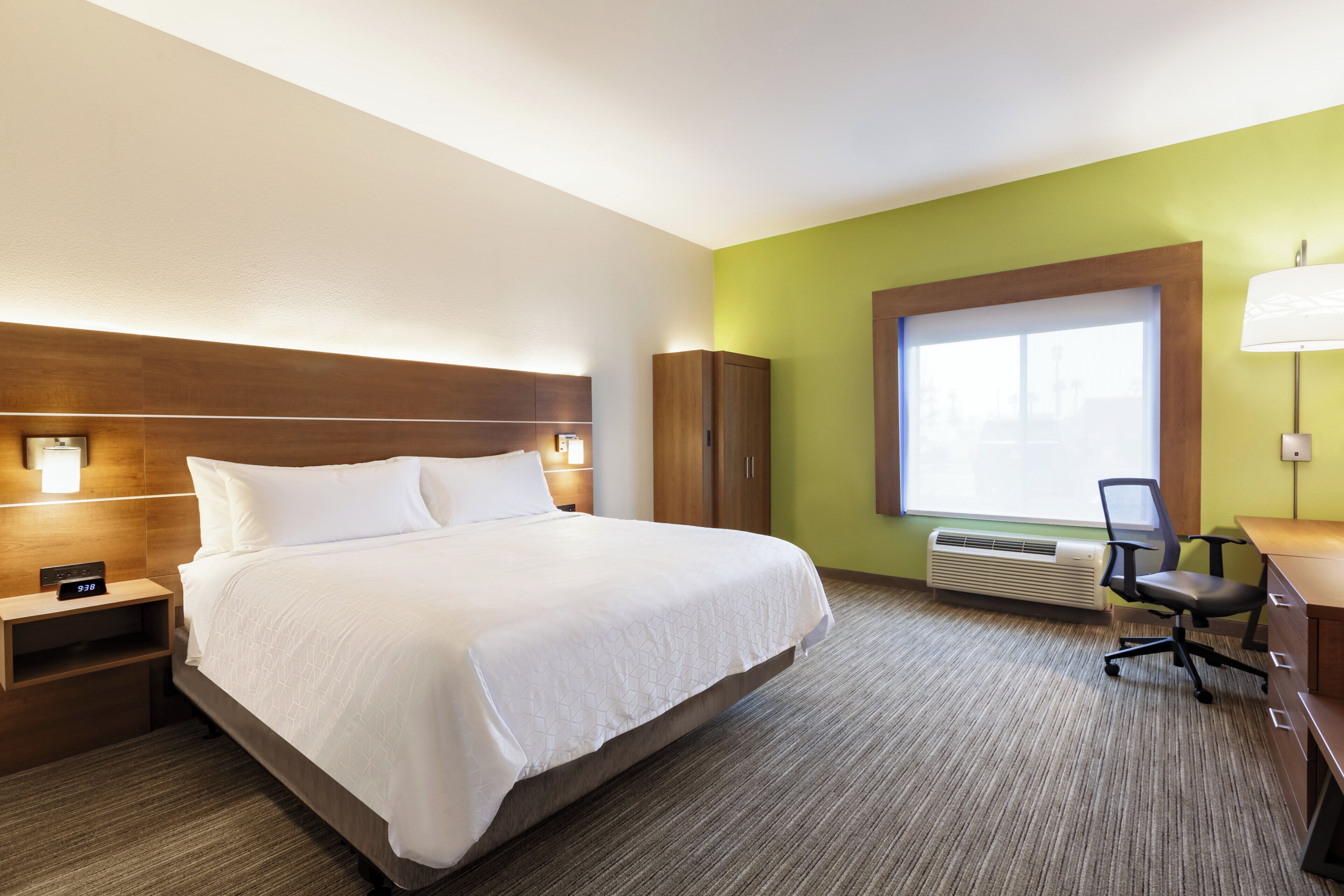 Een hotelkamer met een bed, nachtkastje, bureau, stoel en een groot raam.