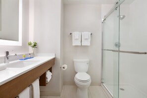 Une salle de bain moderne avec une douche à parois de verre, des toilettes blanches et un meuble-lavabo en bois avec un évier.