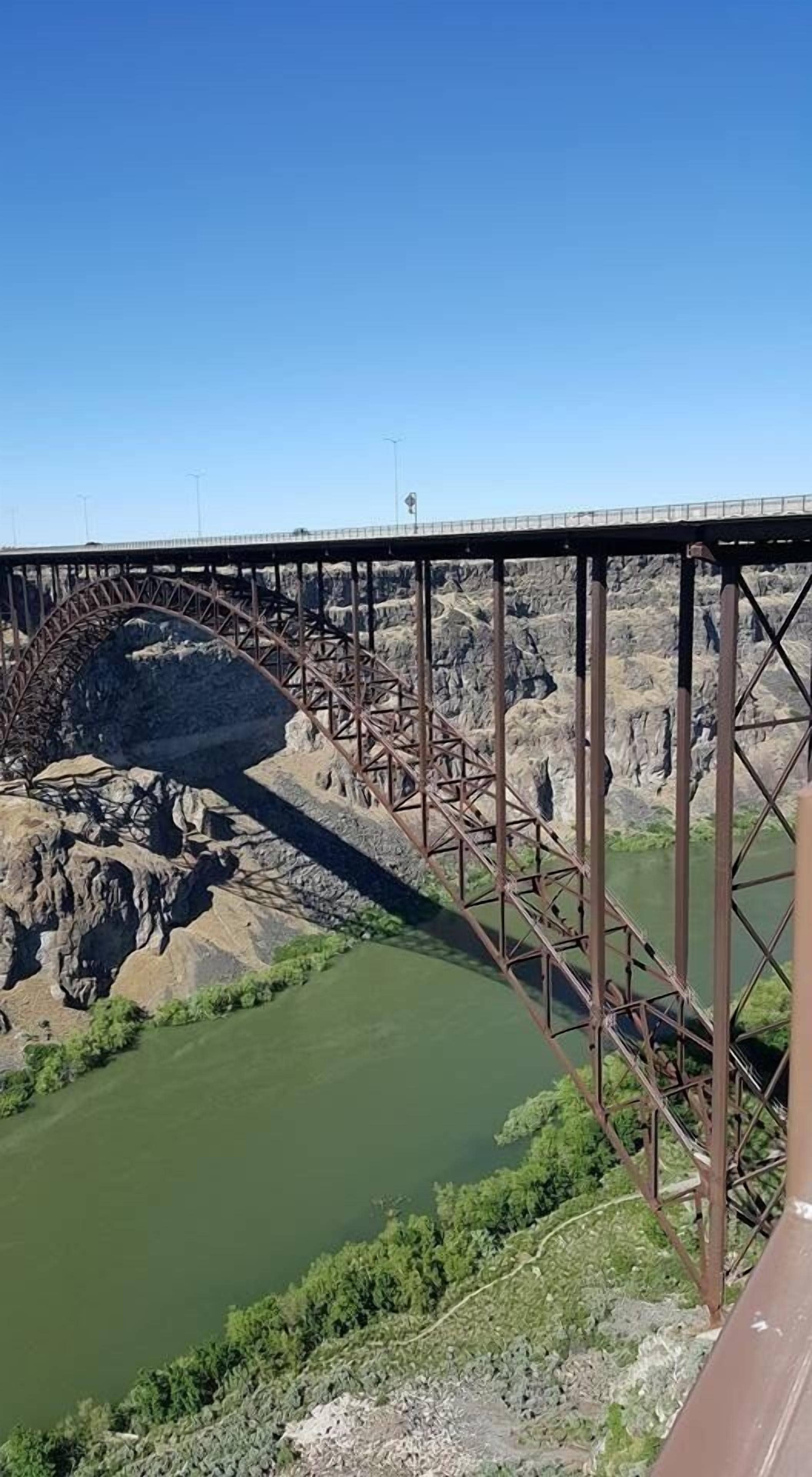 A large metal bridge spanning a river with rocky terrain on either side.