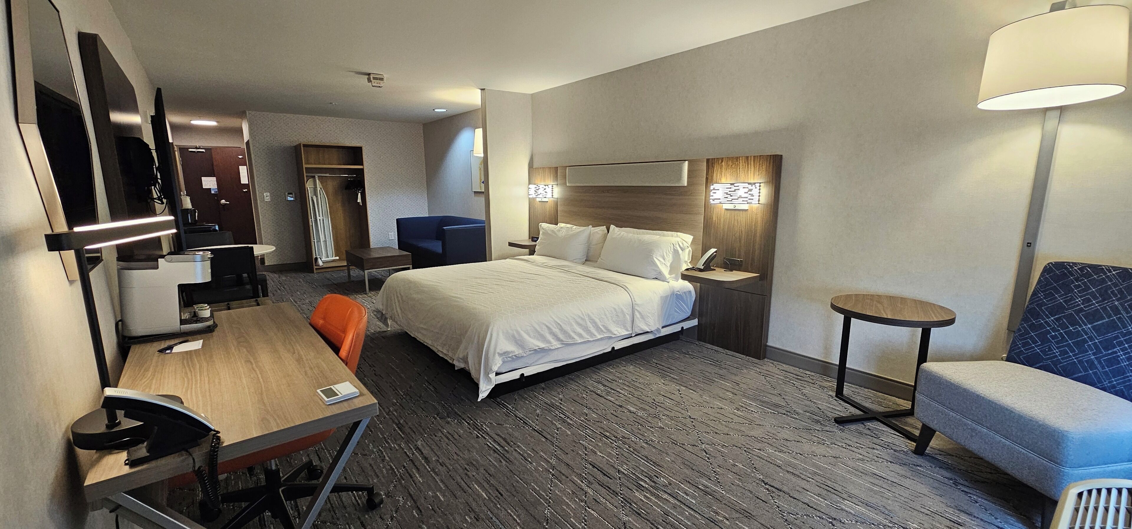 Habitación de hotel con cama, escritorio, silla, mesita y sofá, además de un televisor.