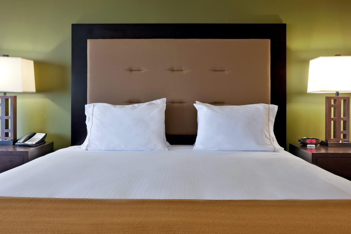 A hotel room with a large bed, two bedside tables, a nightstand, a lamp, a phone, and a clock.