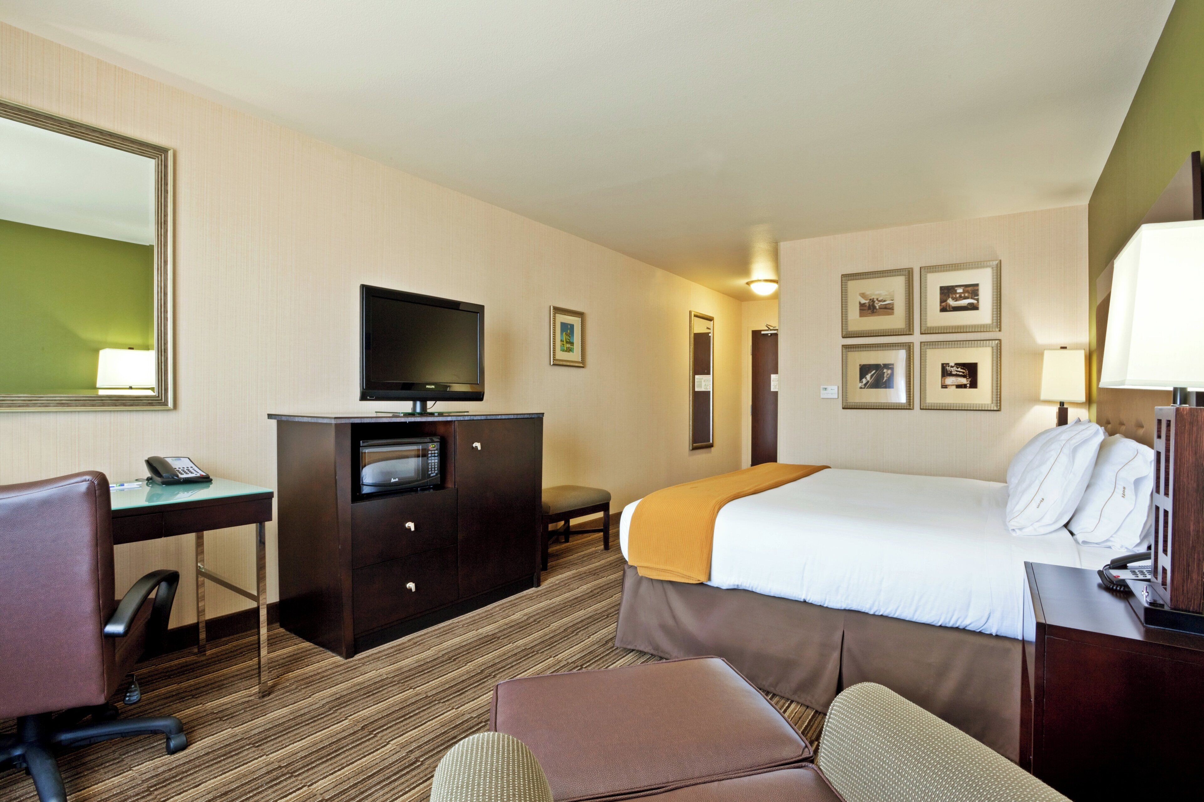 A hotel room with a bed, a desk with a television, a telephone, and a chair.