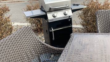 Un espace extérieur aménagé avec un barbecue, des chaises en osier et une table.
