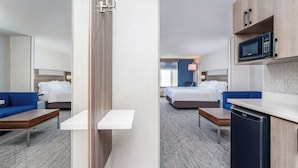 A hotel room with a bed, a blue sofa, a small table, a microwave, and a compact refrigerator. - Holiday Inn Express Hotel & Suites Twin Falls by IHG (Twin Falls)