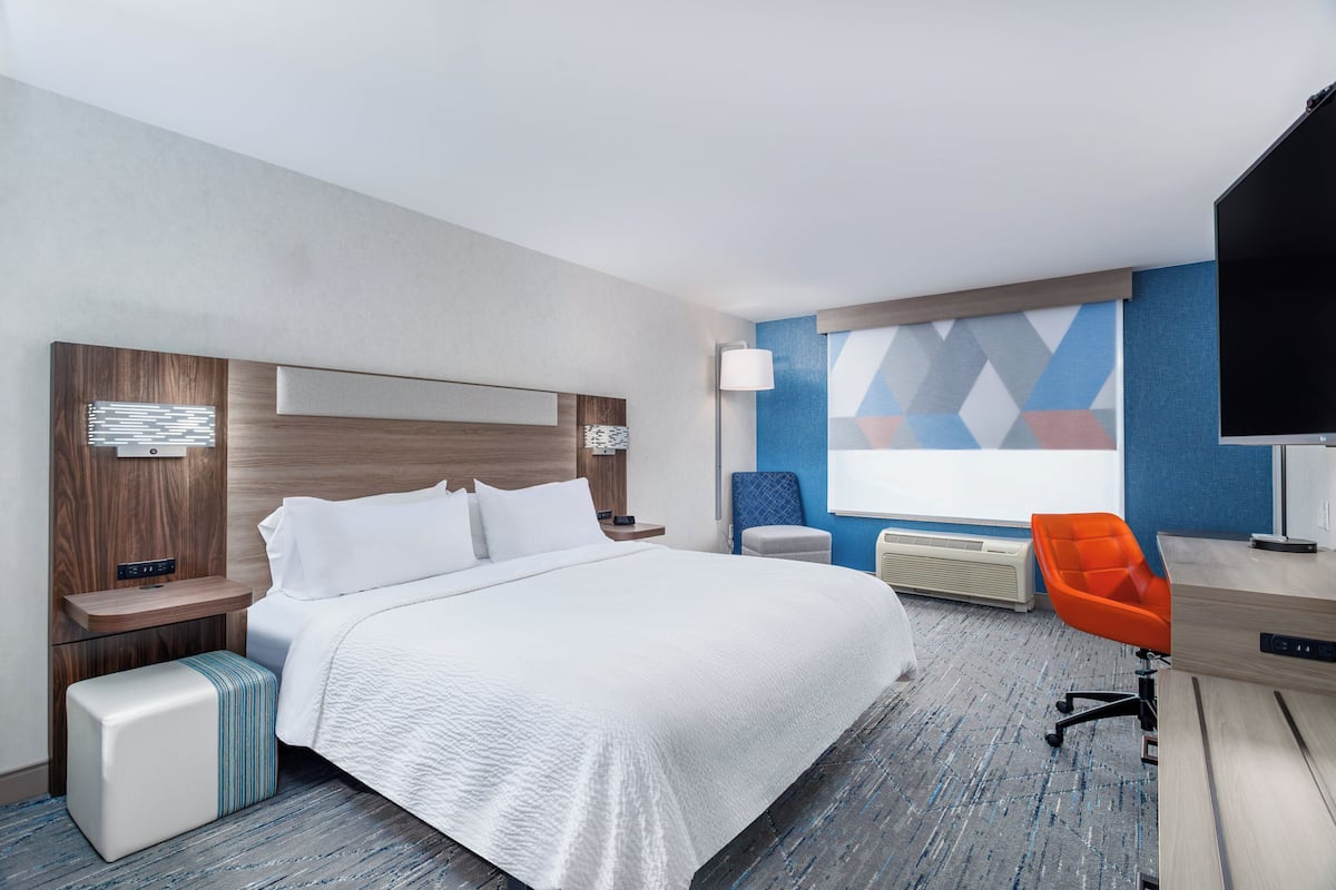A hotel room with a large bed, a desk with a chair, a flat-screen TV, and a wall with a geometric pattern.