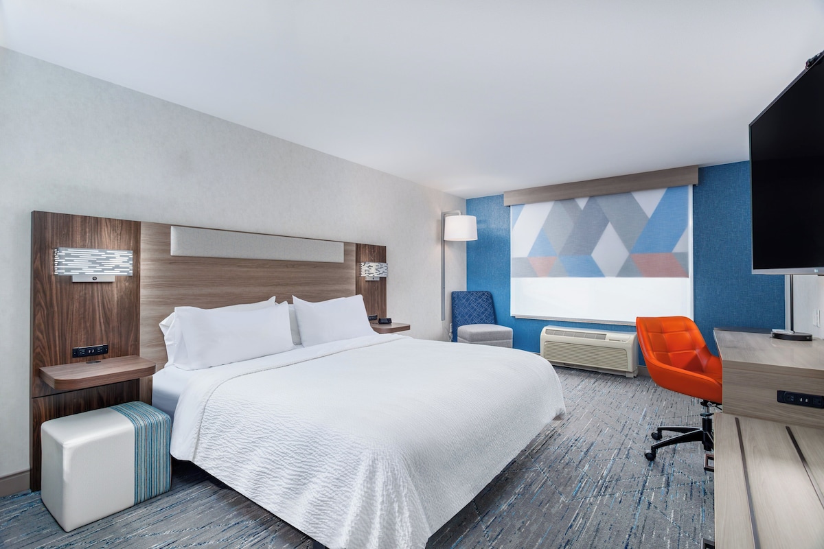 Habitación de hotel con una cama grande, un escritorio con silla, televisor de pantalla plana y una pared con diseño geométrico.