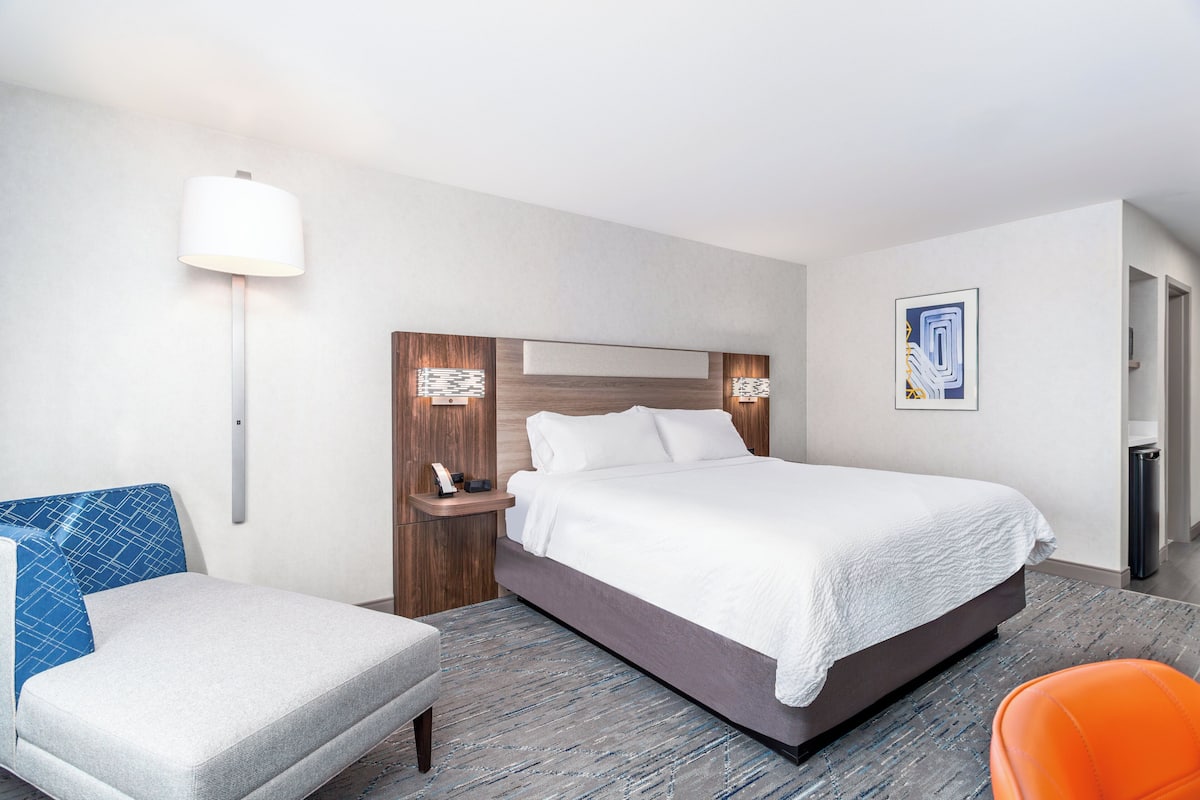 A hotel room with a bed, a nightstand, a chair, and a lamp.