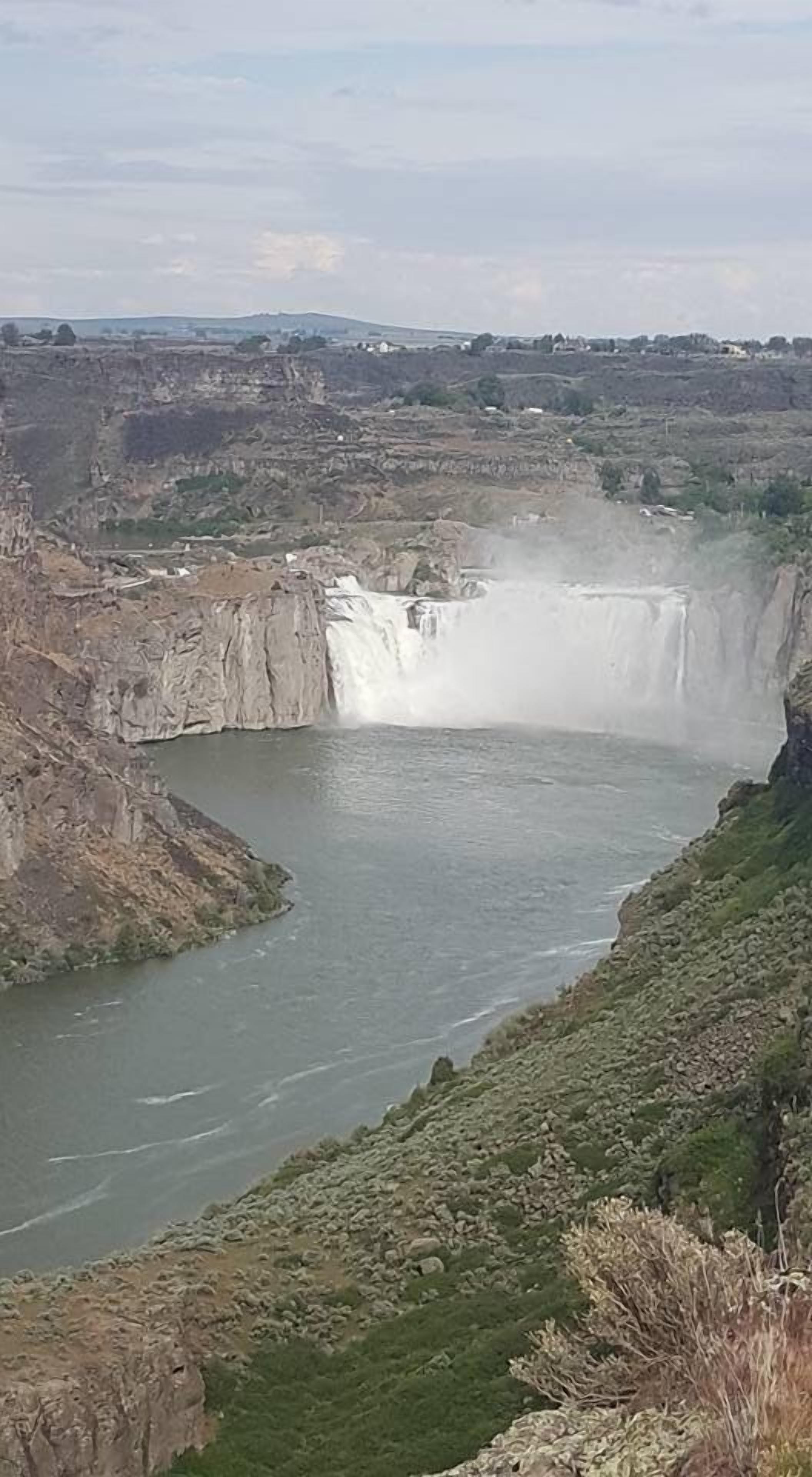 Una cascada grande se precipita a un río, rodeada de terreno rocoso y vegetación escasa.