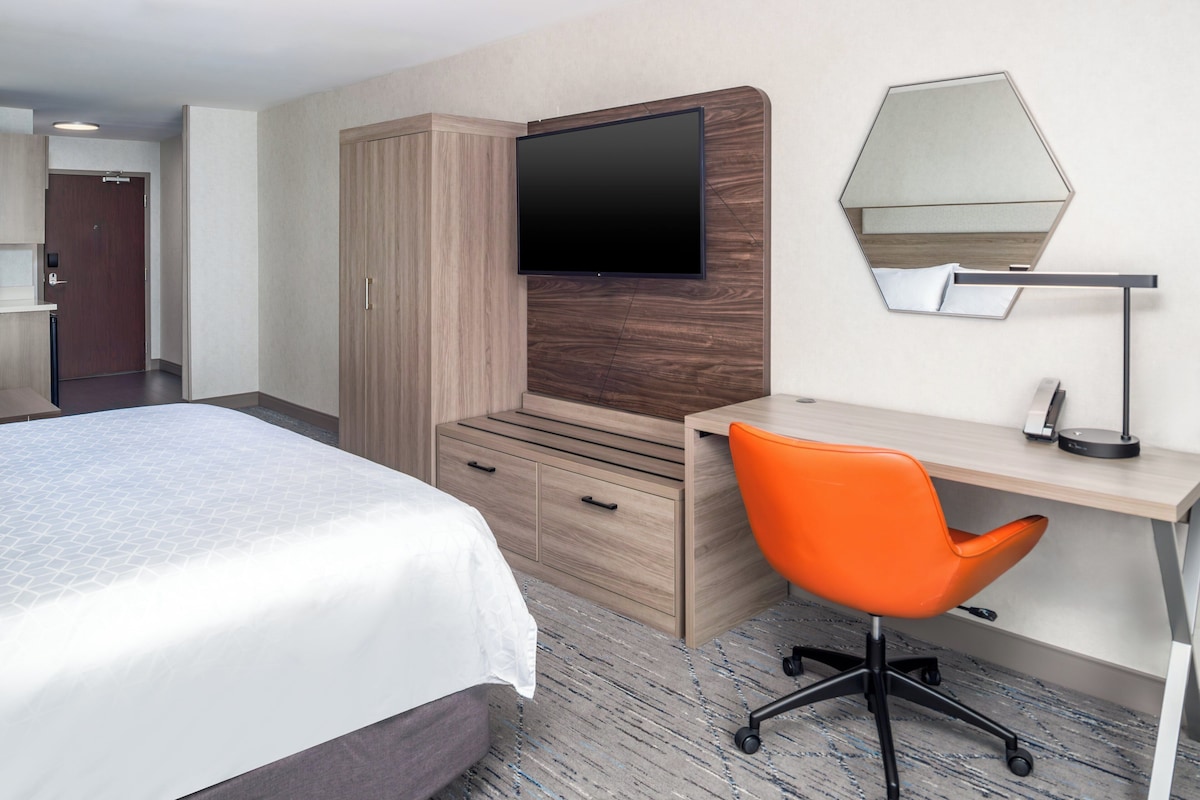 Una habitación de hotel con una cama, un escritorio, una silla naranja, un televisor y un espejo.