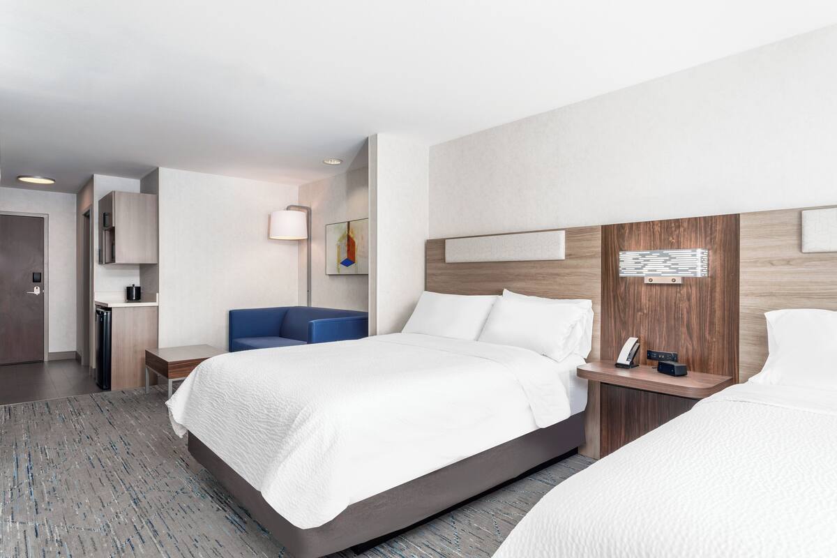 A hotel room with a large bed, a desk, a chair, a small table, a lamp, and a wall-mounted telephone.