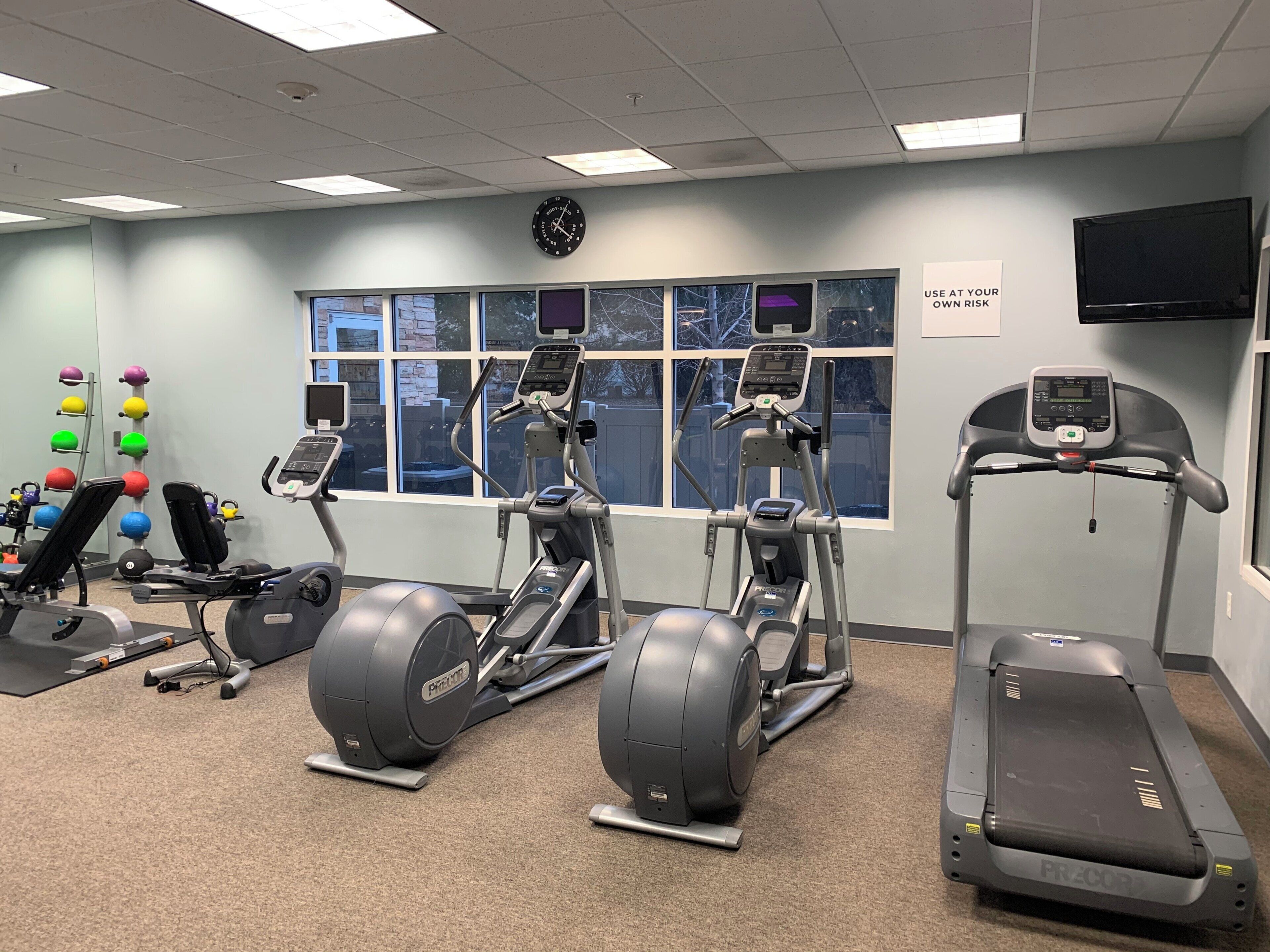 Une salle de sport équipée de tapis de course, de vélos elliptiques et d’une horloge murale.