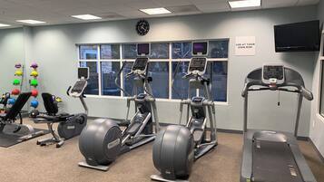 Une salle de sport équipée de tapis de course, de vélos elliptiques et d’une horloge murale.