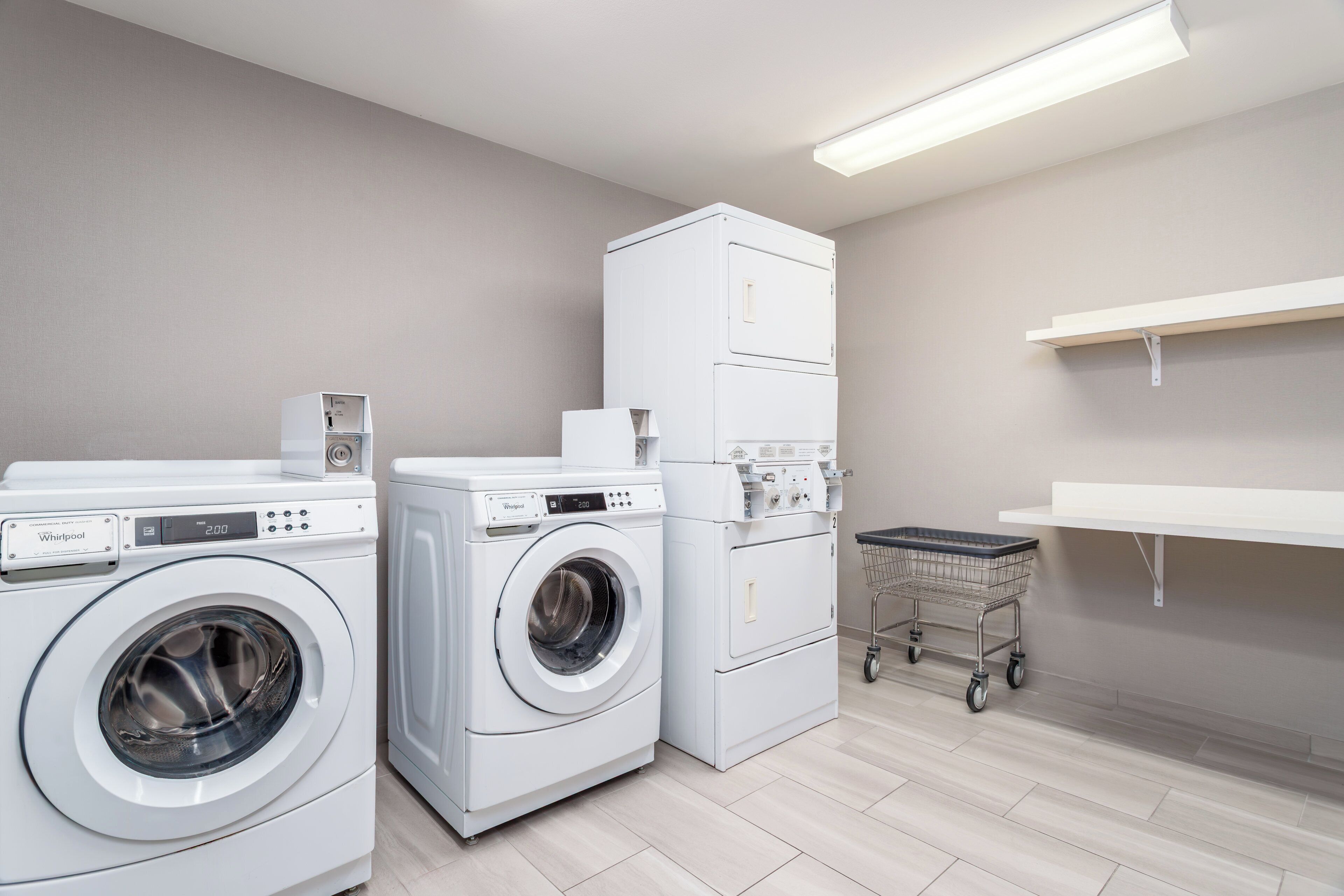 Une buanderie équipée de deux machines  à laver et deux sèche-linge à chargement frontal, d’un chariot et d’une étagère.