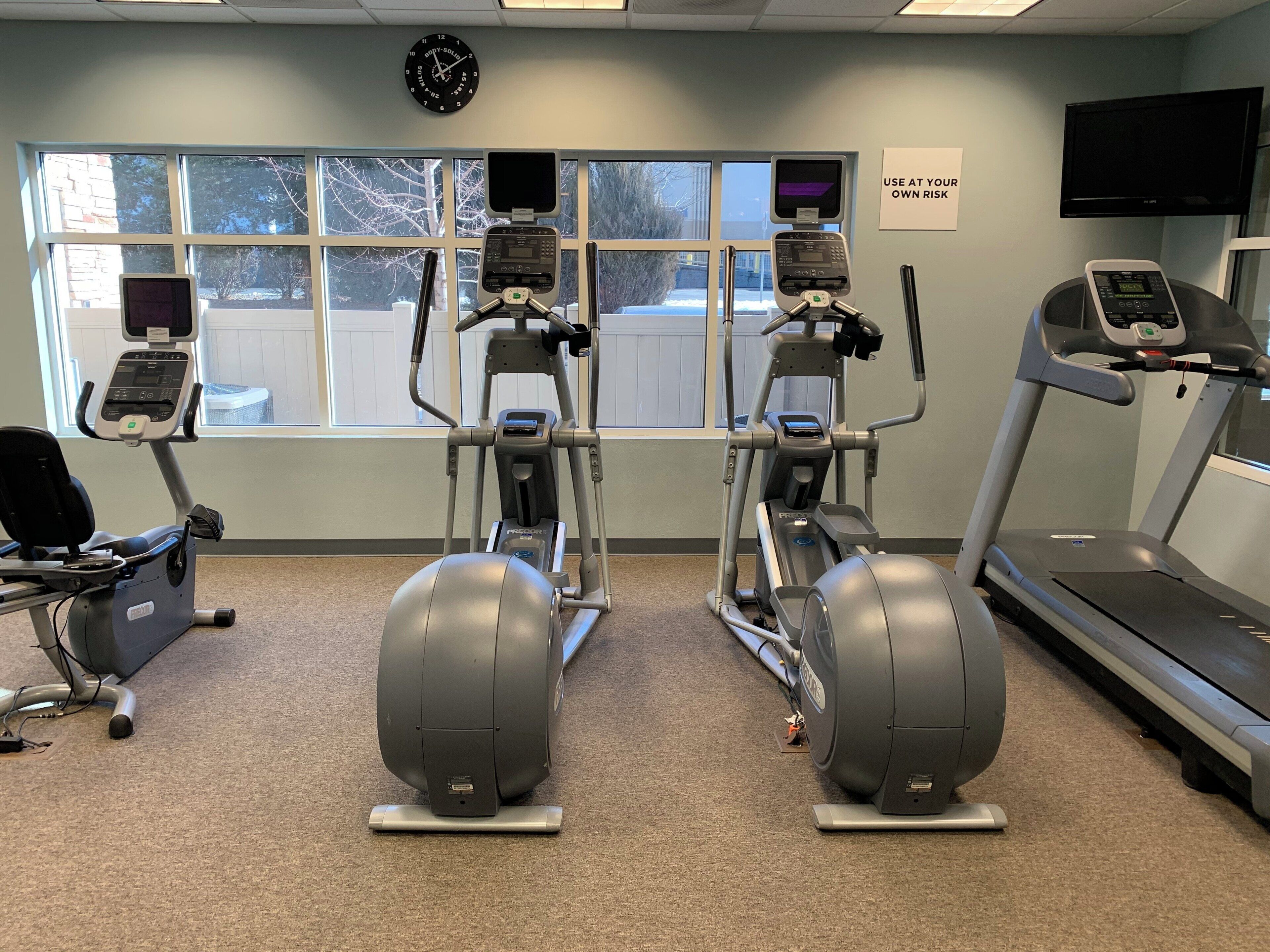 Ein Fitnessstudio mit Laufbändern, Crosstrainern und einem stationären Fahrrad.
