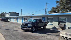 Ein Motel mit blauer Fassade und einer Etage. Vor dem Gebäude ist ein dunkel gefärbter Pick-up geparkt.
