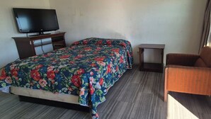 Ein Zimmer mit einem Bett, einem Fernseher auf einem Schrank, einem kleinen Tisch und einem Sessel.