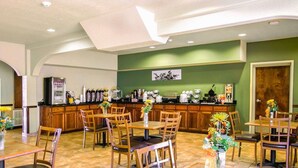 A restaurant with wooden tables and chairs, a counter with a coffee machine, and a green wall with a framed picture. - Sleep Inn & Suites Gonzales near Palmetto State Park (Gonzales)