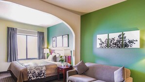 A hotel room with a bed, a sofa, a coffee table, and a wall with a floral artwork. - Sleep Inn & Suites Gonzales near Palmetto State Park (Gonzales)