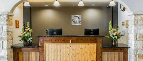 A reception desk with a wooden panel design, two black computers, and a sign that reads "Sleep Inn & Suites."