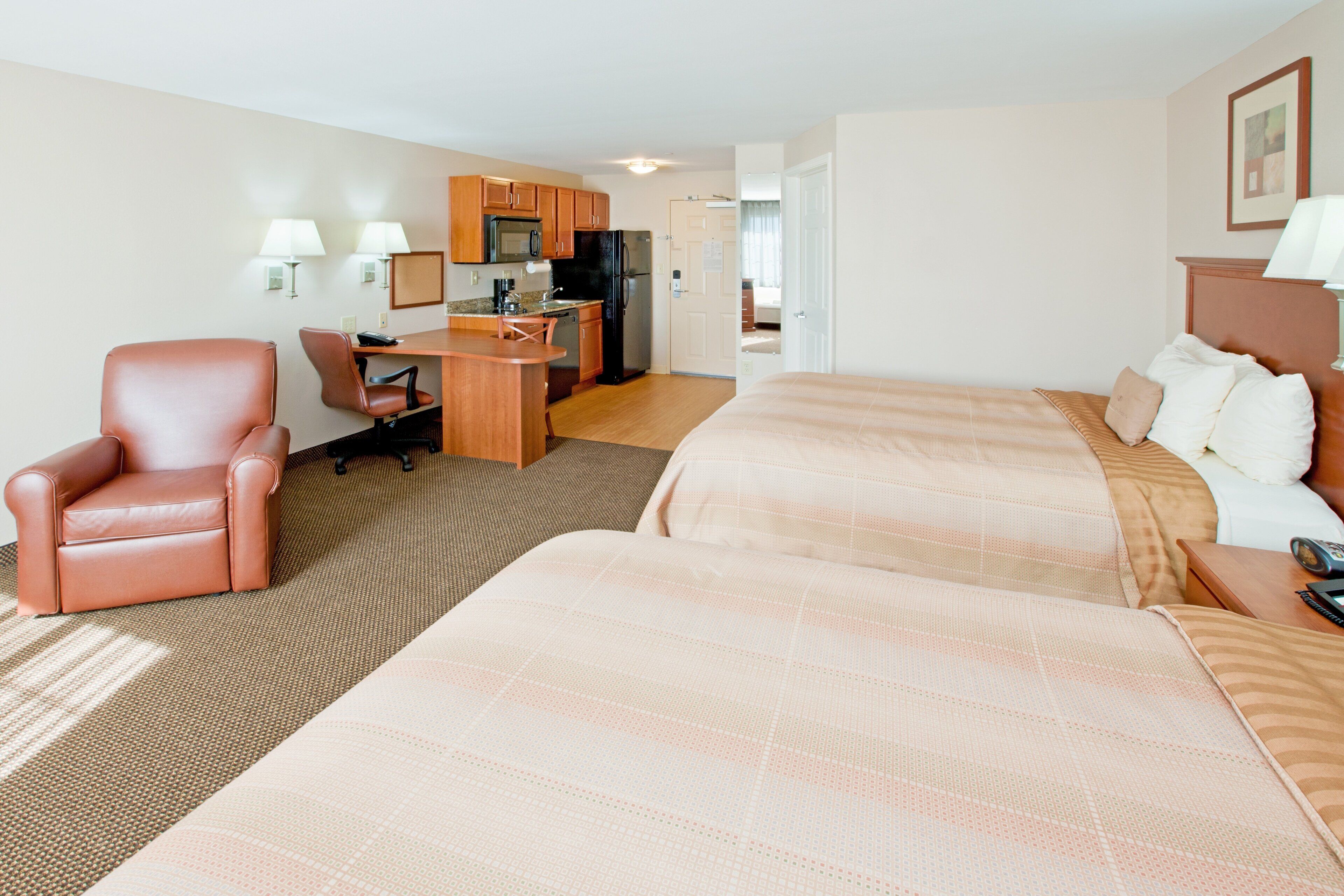 A hotel room with a bed, a desk, a chair, and a kitchenette.