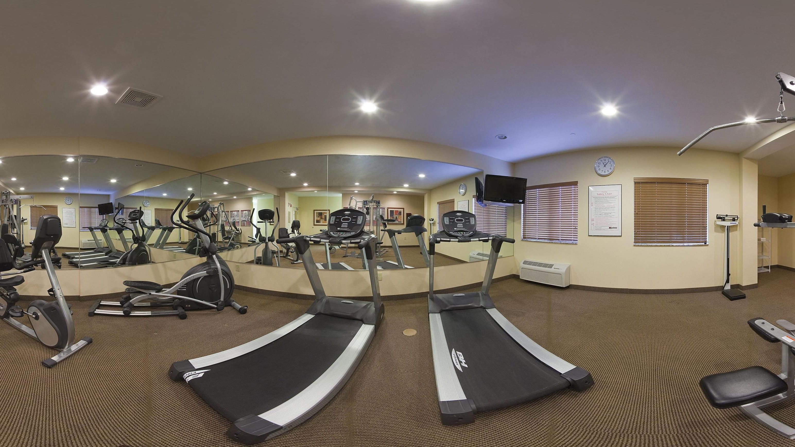 Une salle de sport équipée de tapis de course, de vélos d’exercice et d’un mur recouvert de miroirs.