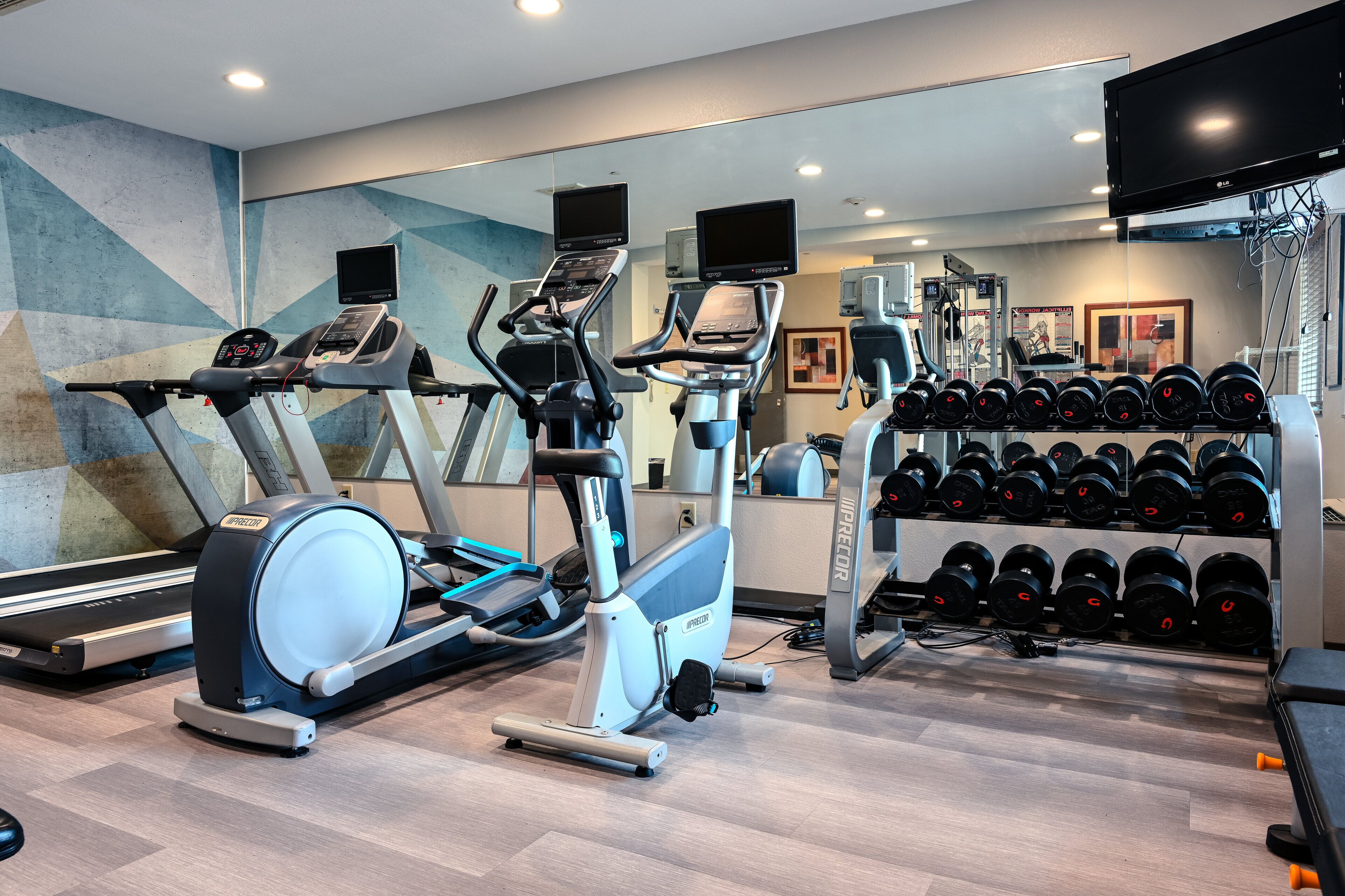 Een fitnessruimte met loopbanden, elliptische trainers en een rek met dumbbells.