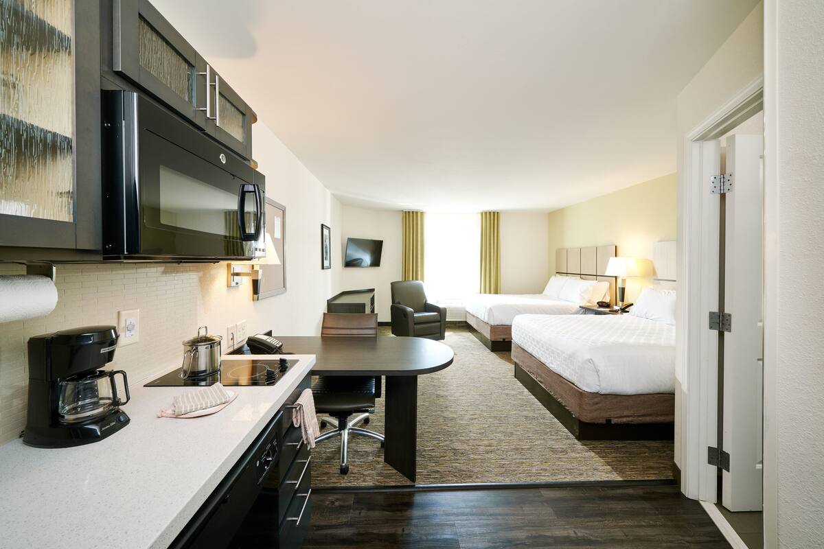 A hotel room with a kitchenette, a bed, a desk, and a chair.