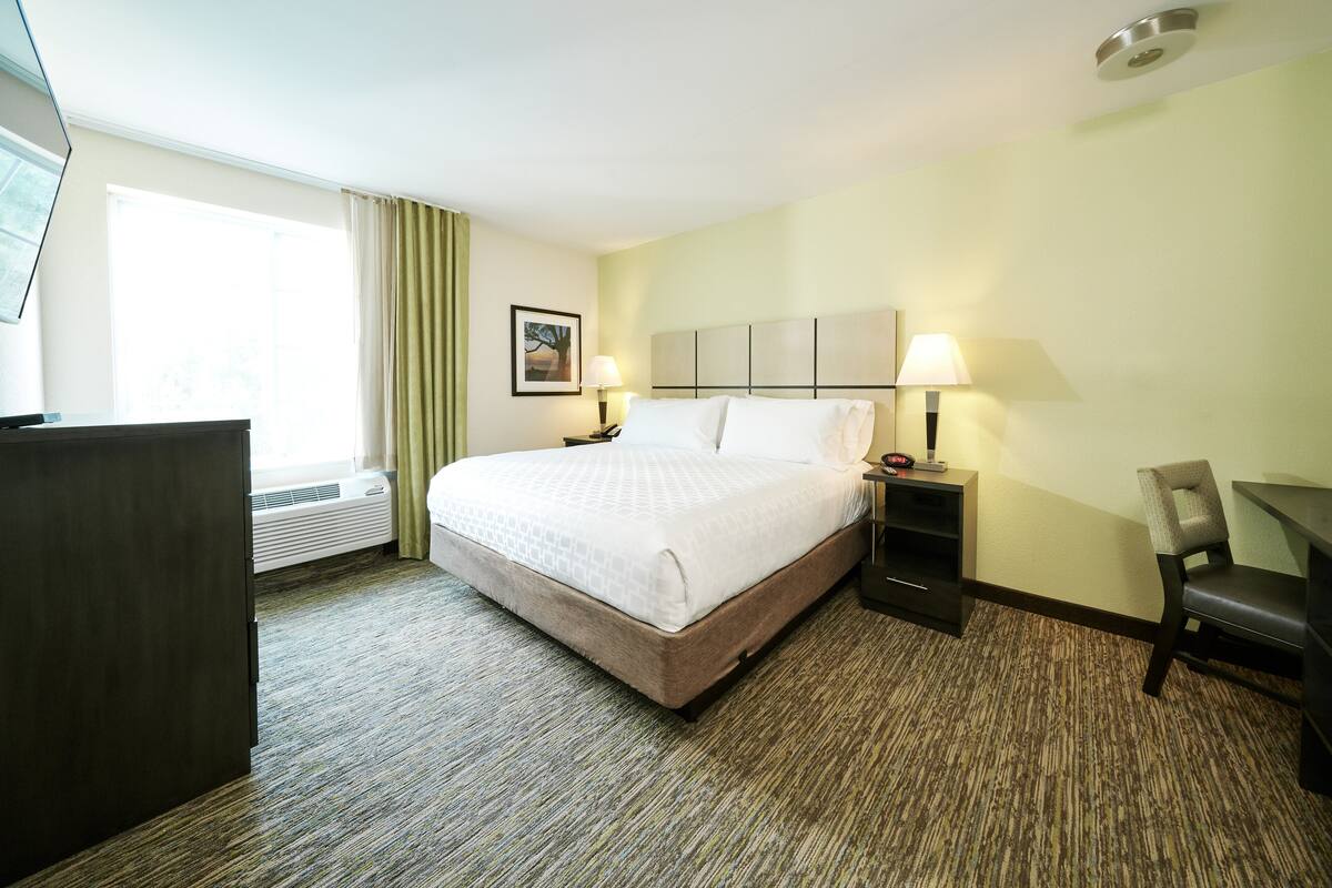 A hotel room with a large bed, two bedside tables with lamps, a desk, a chair, and a window with curtains.