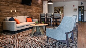 A modern lobby with a wooden wall, a sofa with orange cushions, a round coffee table, and a blue armchair. - Candlewood Suites Lafayette by IHG (Lafayette)