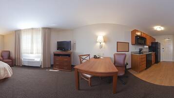 Een hotelkamer met een eettafel, stoelen, een televisie, een kitchenette en een bed.