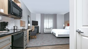Una habitación de hotel compacta con kitchenette, una cama, un escritorio y un televisor.