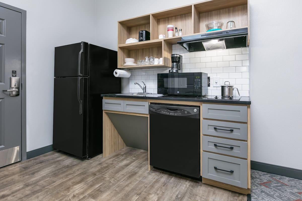 Una cocina compacta con un refrigerador negro, un microondas, un lavavajillas y estantes de madera sobre la encimera.