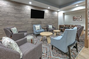 Un área de estar moderna con sillones tapizados de color gris, un televisor de pantalla plana montado en la pared y una alfombra estampada.
