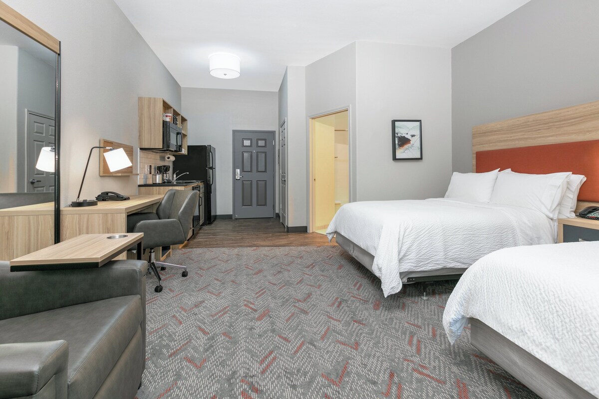 Una habitación de hotel con una cama, un escritorio con computadora, una silla, una mesita y un microondas.