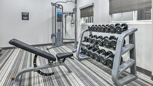 Un gimnasio con equipo de levantamiento de pesas, mancuernas y una banca.