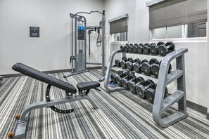 Un gimnasio con equipo de levantamiento de pesas, mancuernas y una banca.