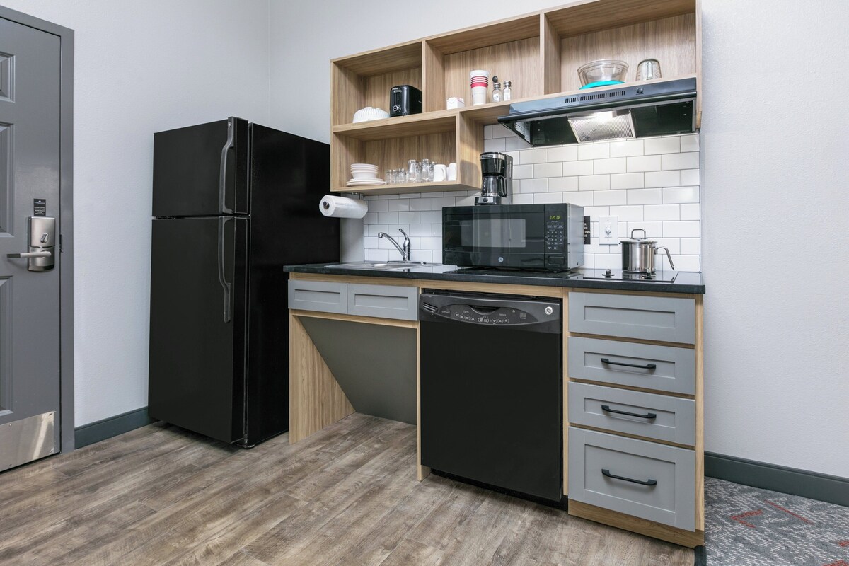 Una cocina compacta con un refrigerador negro, un microondas, un lavavajillas y estantes de madera sobre la encimera.