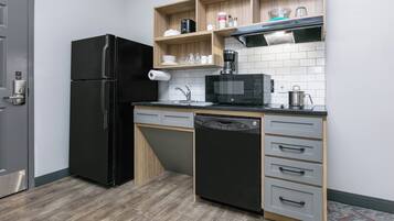 Eine kleine Küche mit einem schwarzen Kühlschrank, einer Mikrowelle und einem Geschirrspüler.