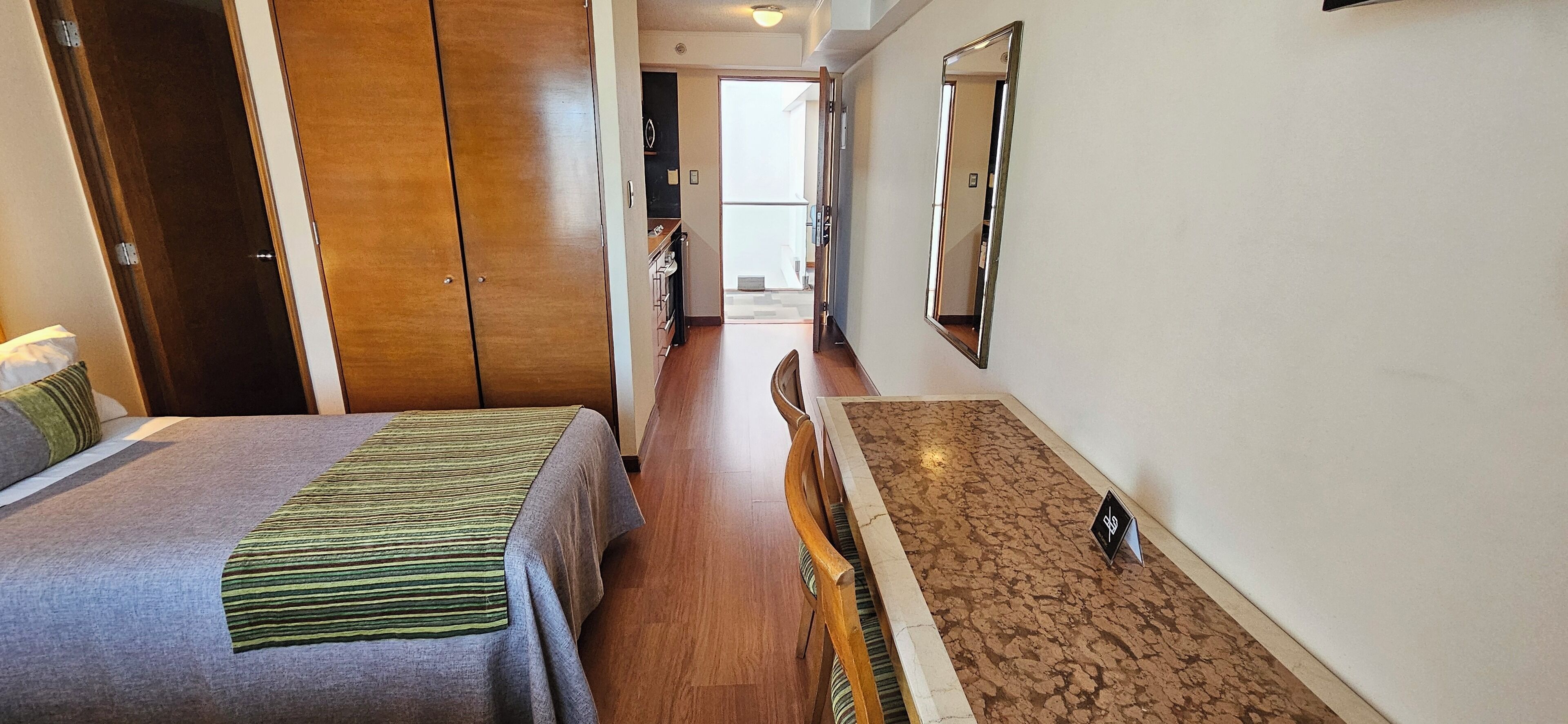 A hotel room with two beds, a wooden wardrobe, a mirror, and a small table with a bottle.