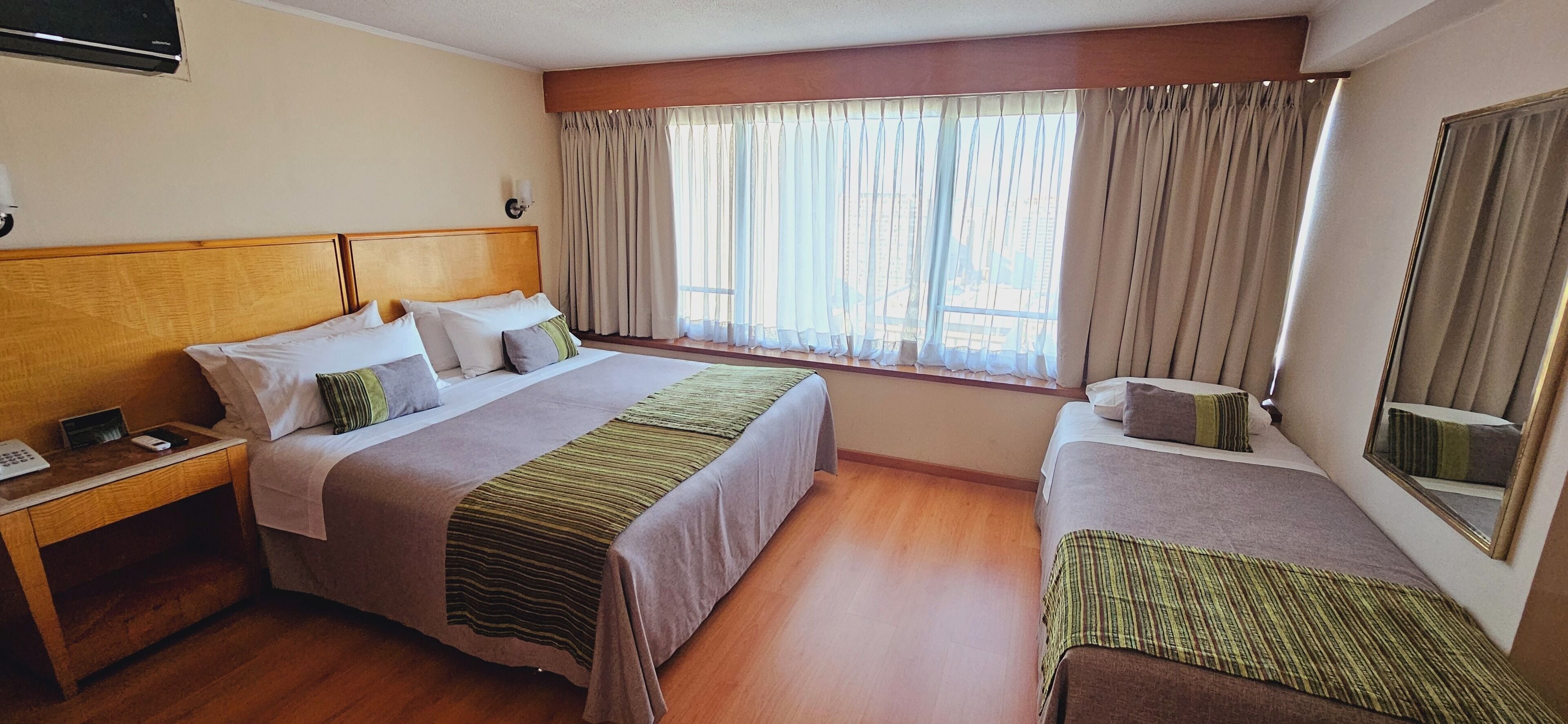 Een hotelkamer met twee bedden, een houten hoofdbord, een nachtkastje en een raam met gordijnen.