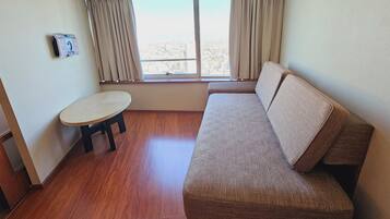 Una habitación con sofá, una mesita redonda, ventana con cortinas y aire acondicionado de pared.