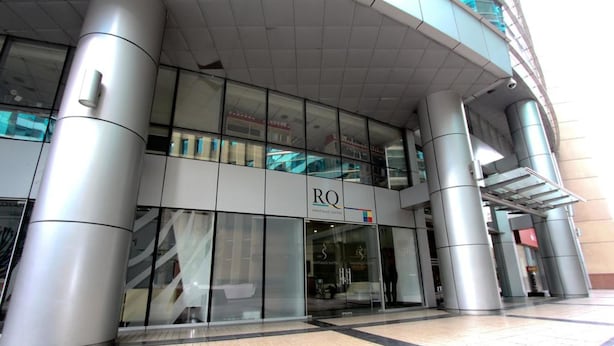 Een modern gebouw met een glazen gevel en een bordje met de tekst 'RQ'.