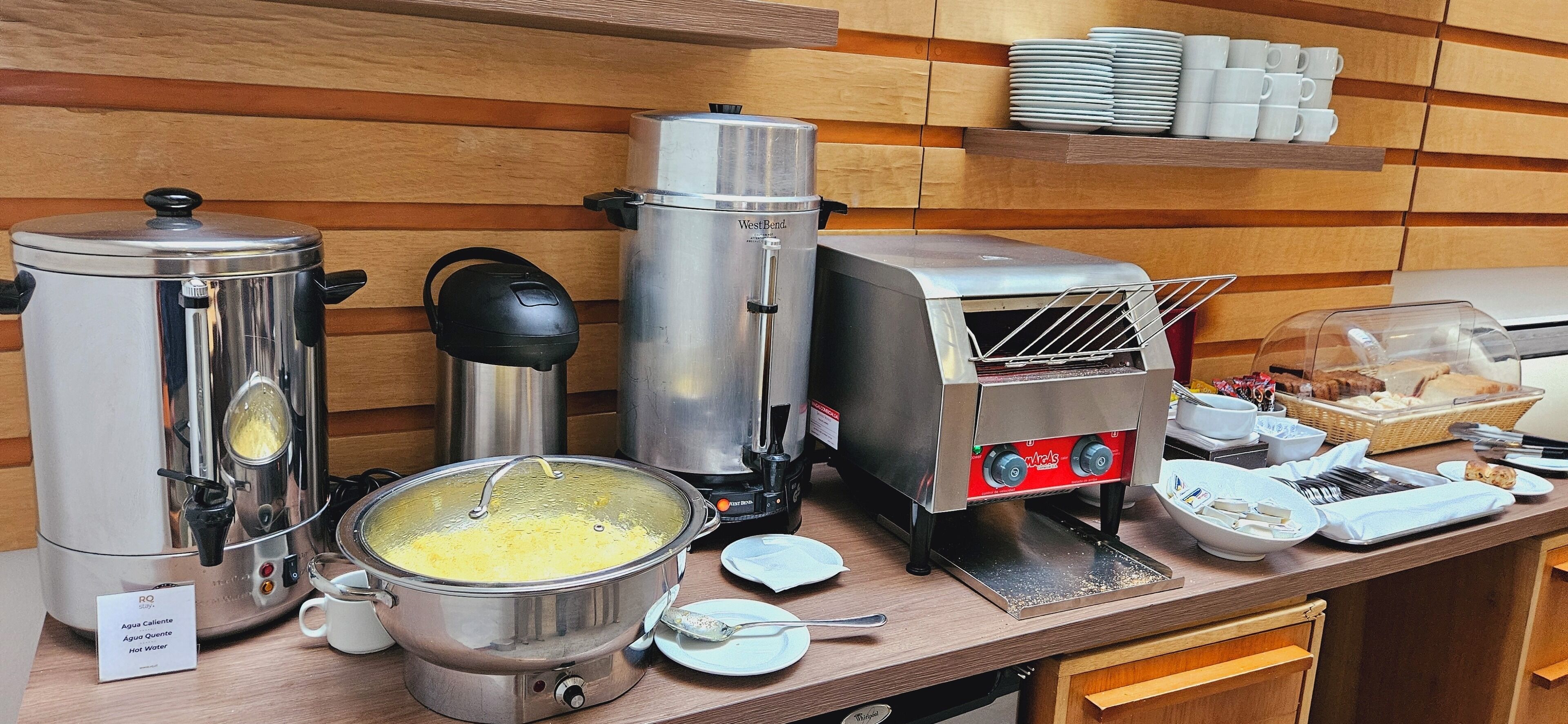 Una zona de cocina con cafetera, dispensador de agua caliente, tostadora y un montaje tipo bufé.